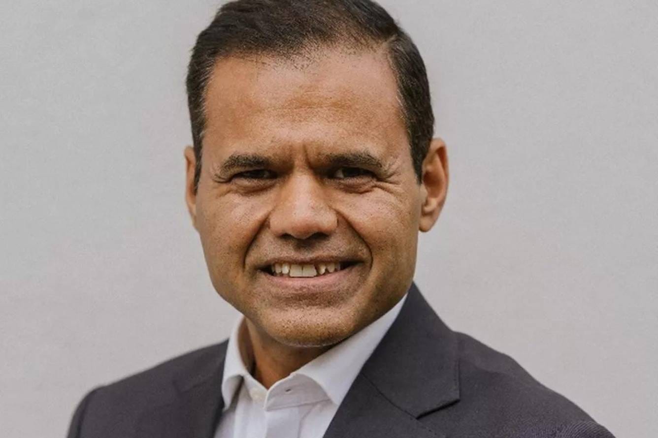Photograph of Rajesh Agrawal smiling at the camera. It is an official portait, with a plain background. He is wearing a suit without a tie.