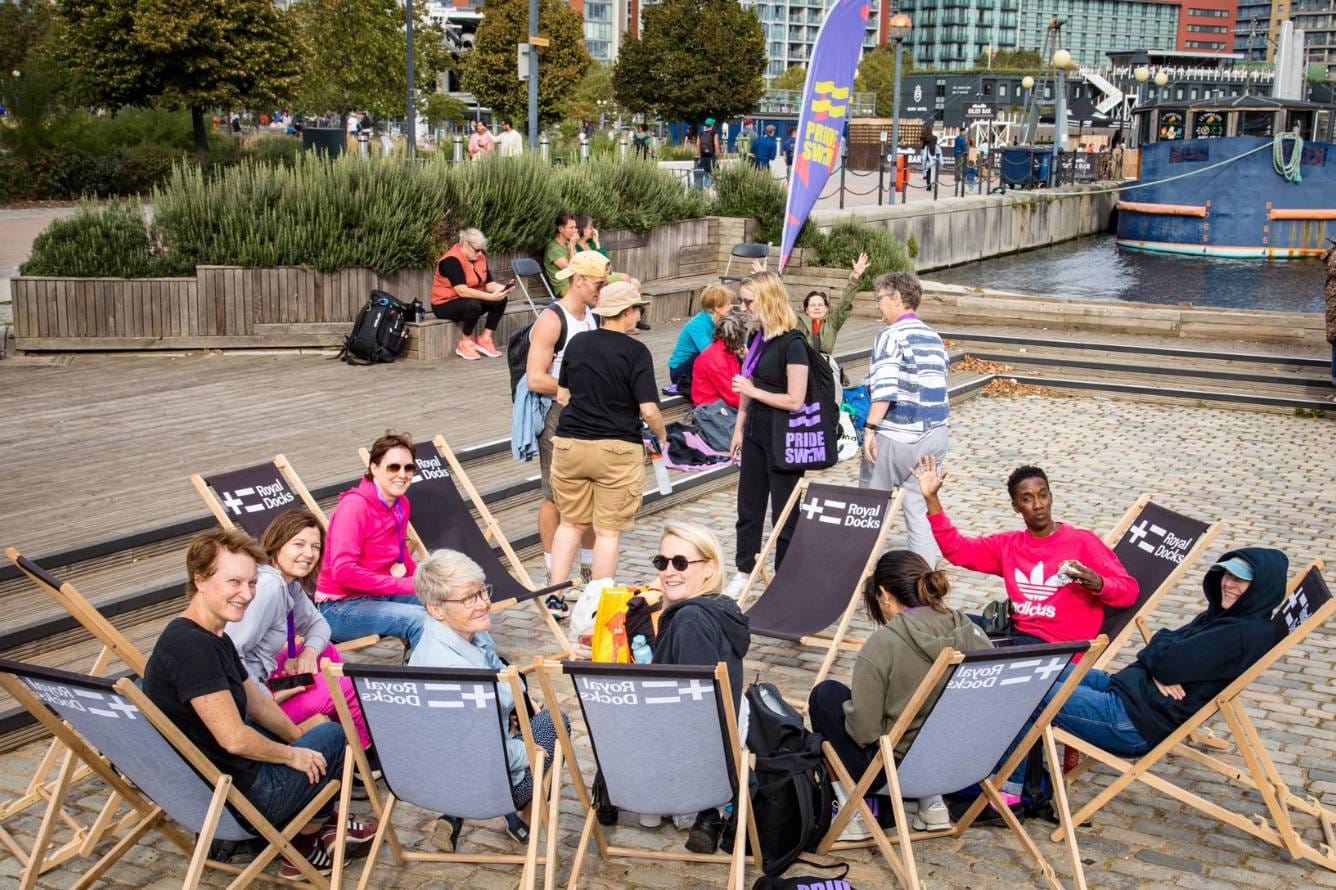 People sit on deck chairs in a circle. They are looking at the camera and smiling.