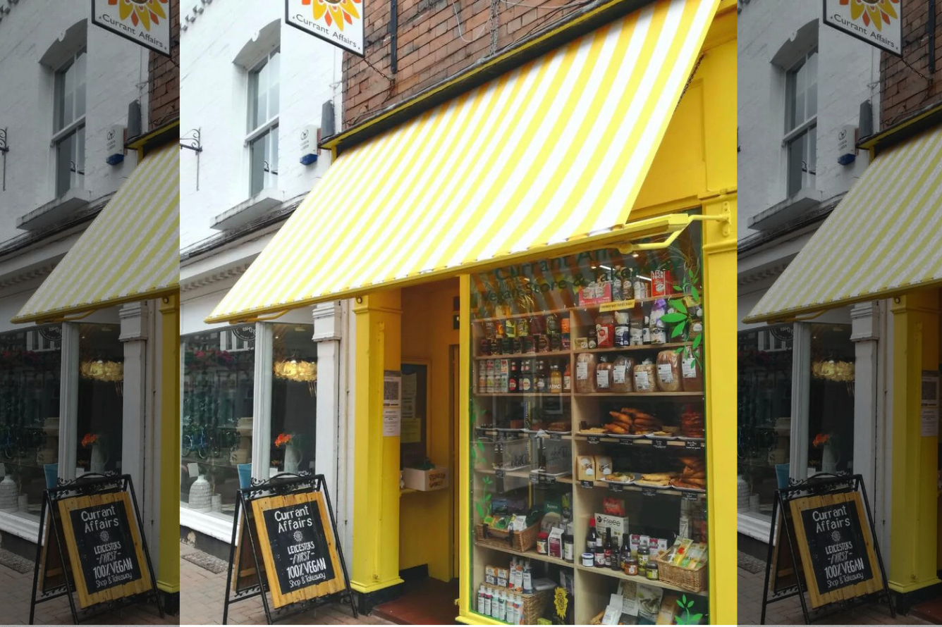 Pictured is the shop front of Current Affairs, Vegan shop. The building and signage are bright yelloe and green. 